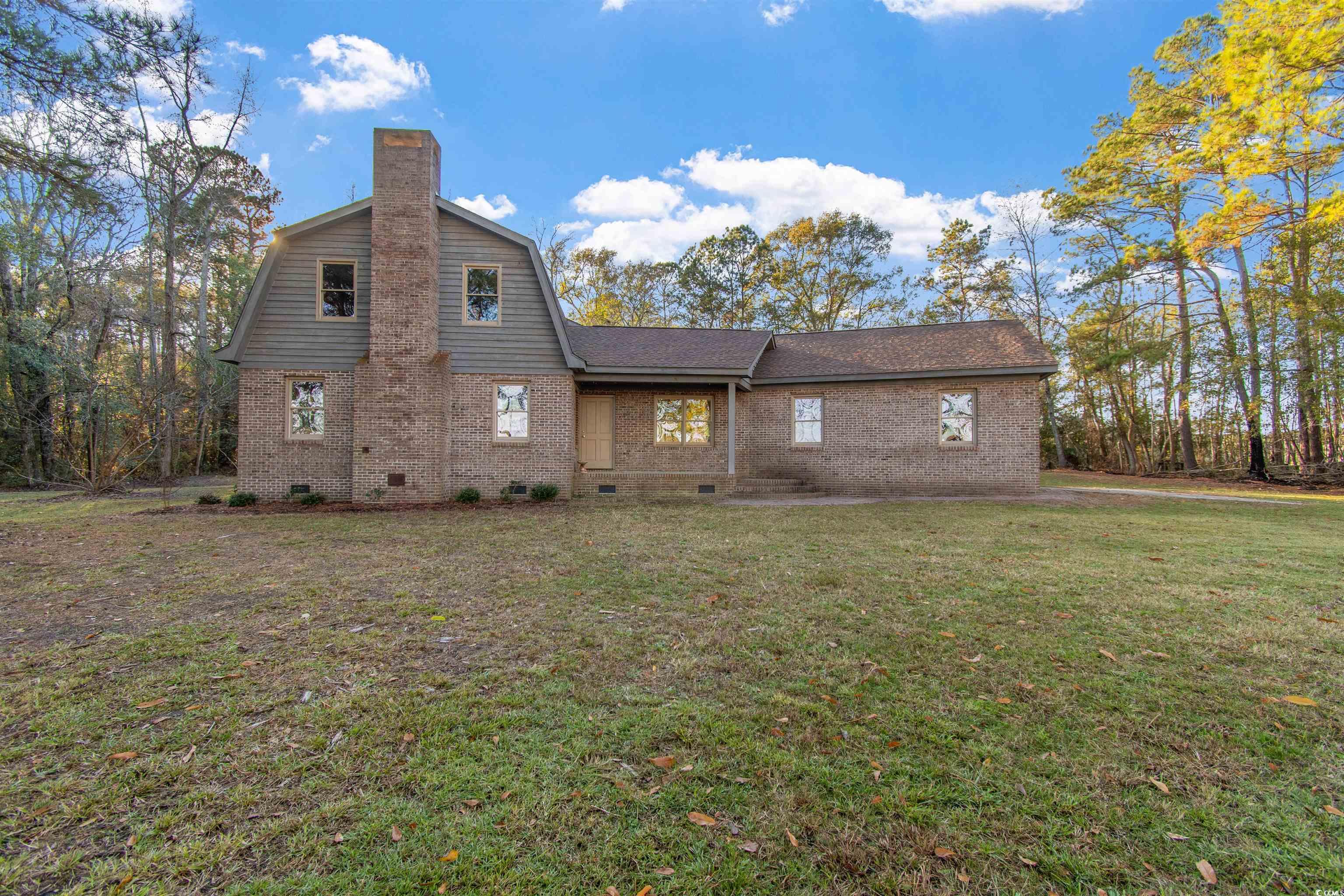 Front of house with crawl space, brick siding, a yard, a gambrel roof, and a chimney
