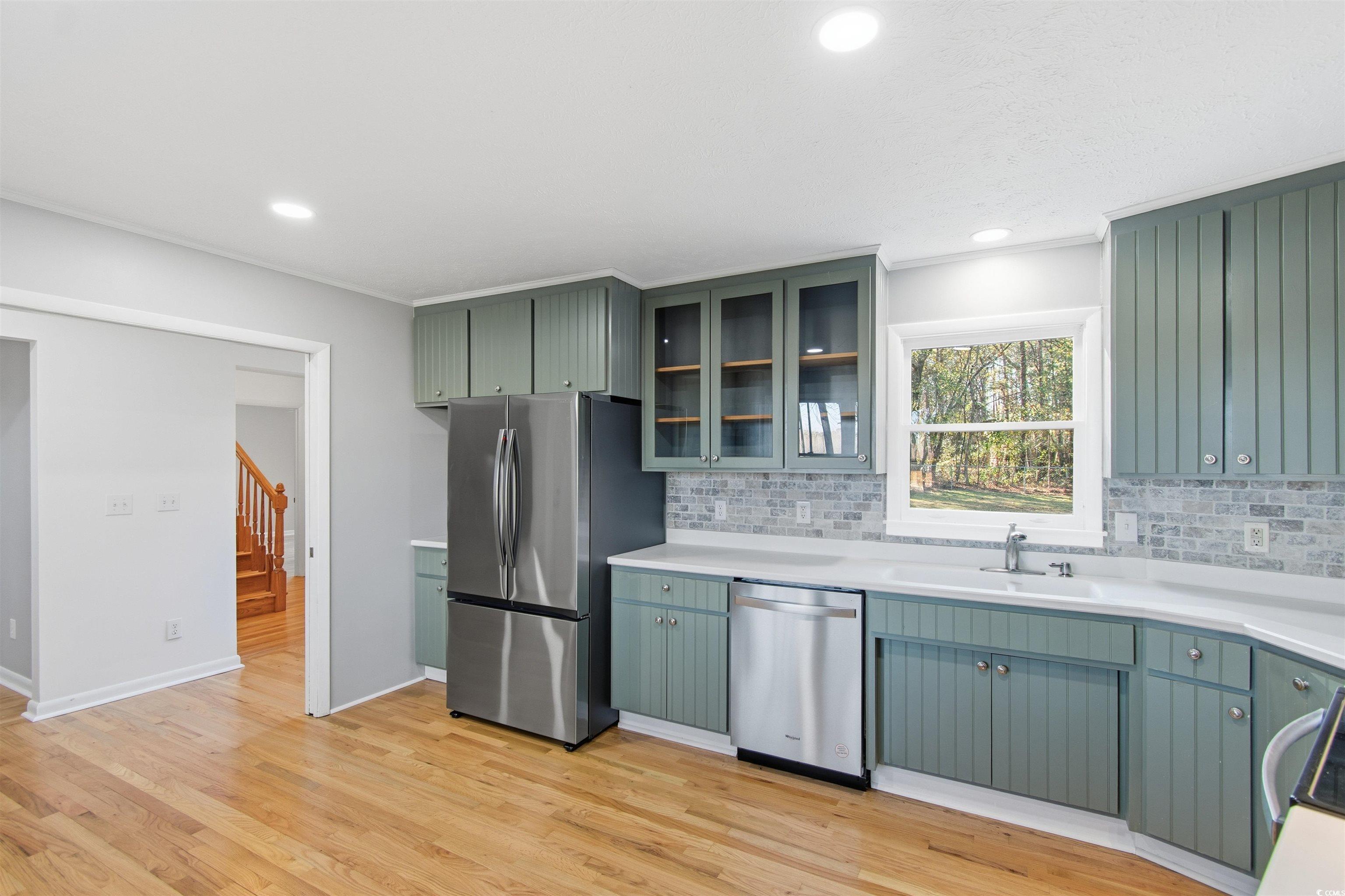 50 Irvin Enzor Road North Fair Bluff, NC 28439 - Photo 9 of 26 Kitchen featuring green cabinetry, appliances with stainless steel finishes, glass insert cabinets, light wood finished floors, and tasteful backsplash