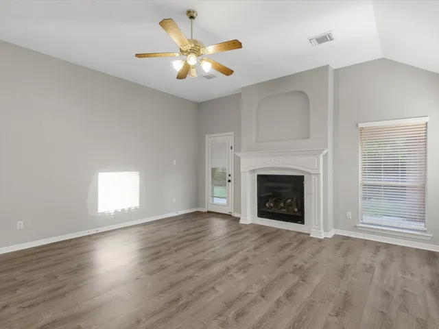 an empty room with windows fireplace and a kitchen view