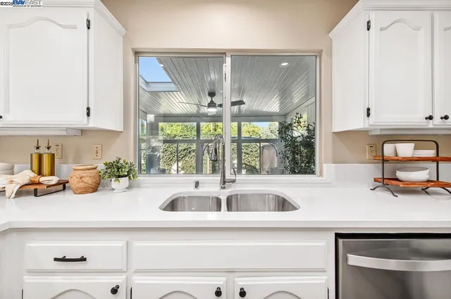 a large white kitchen with granite countertop a white stove a sink and white cabinets with wooden floor
