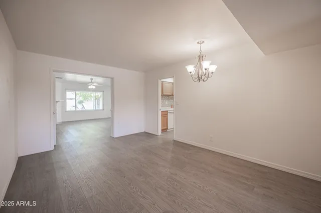 an empty room with wooden floor chandelier and windows
