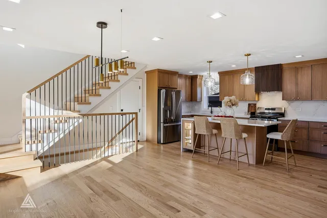 a open kitchen with stainless steel appliances kitchen island granite countertop a refrigerator a stove a sink and a dining table with wooden floor