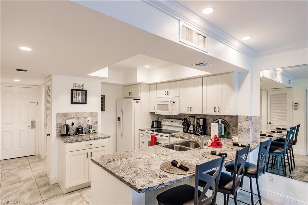 600 Neapolitan Way, Unit 454 Naples, FL 34103 - Photo 9 of 26 a kitchen with kitchen island a stove a table and chairs in it