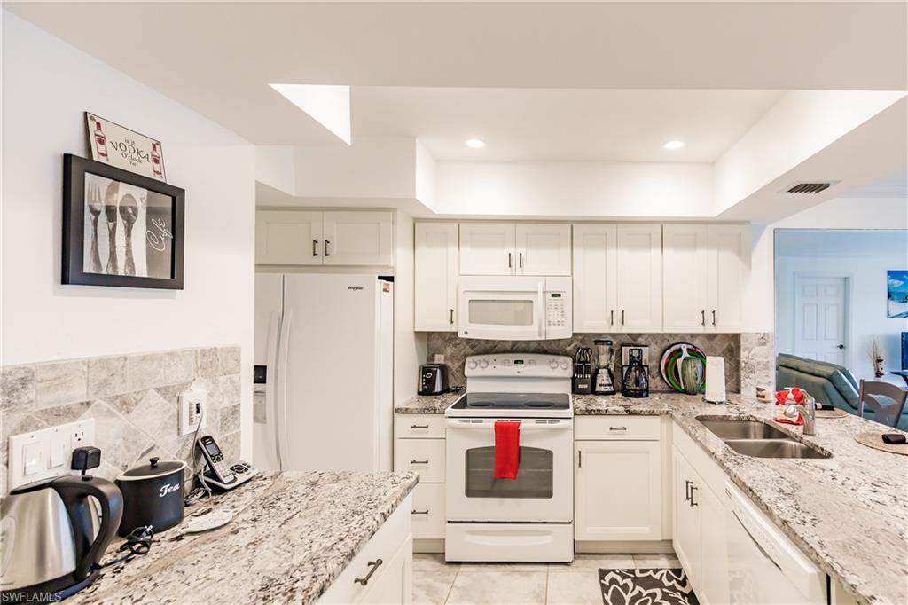 600 Neapolitan Way, Unit 454 Naples, FL 34103 - Photo 10 of 26 a kitchen with stainless steel appliances kitchen island granite countertop a sink refrigerator and cabinets