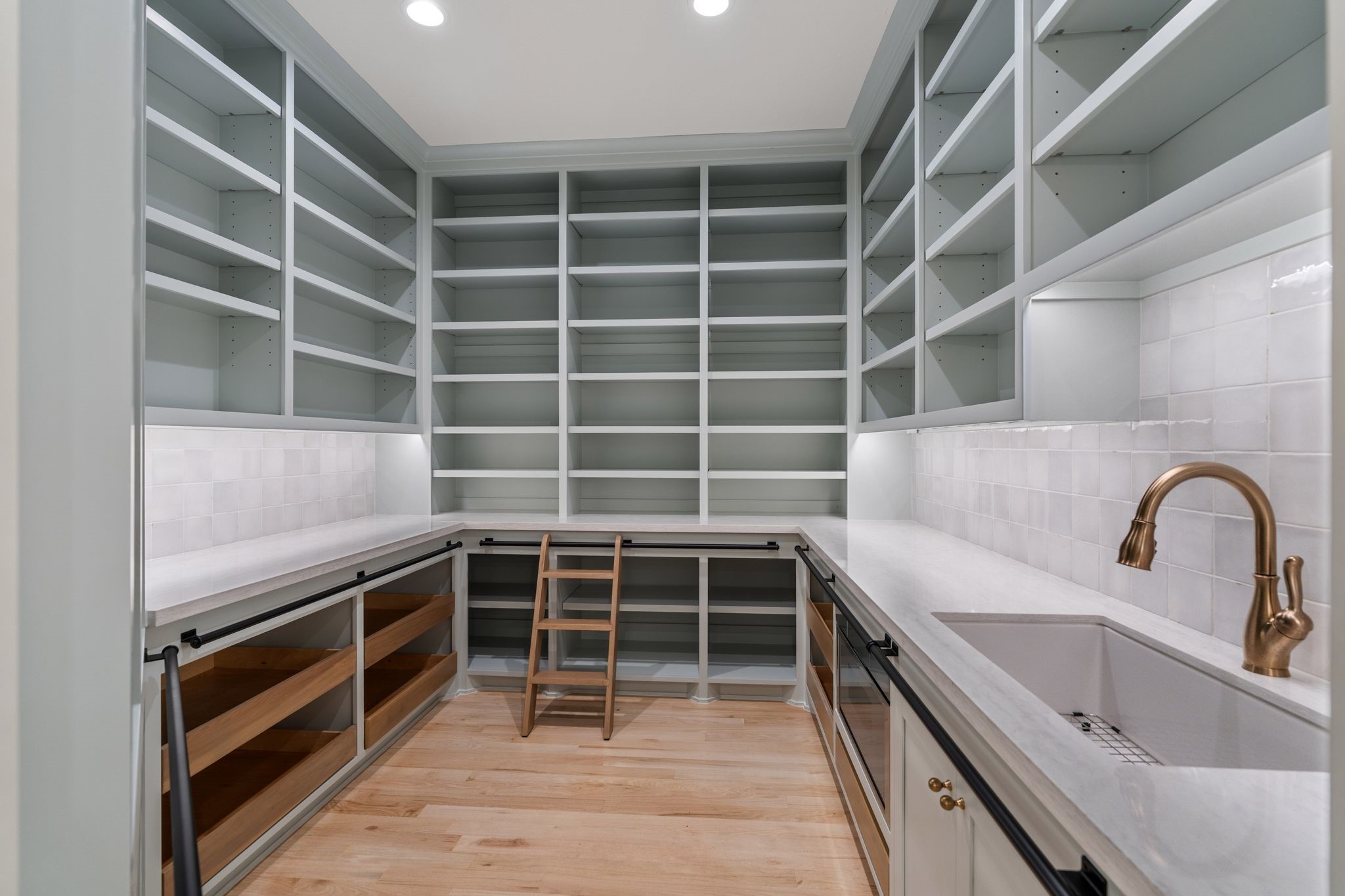 31 Hollymead Drive Spring, TX 77381 - Photo 16 of 50 This photo showcases a spacious, well-designed walk-in pantry with ample shelving, marble countertops, a sink, and a microwave. It features under-cabinet lighting, pull out shelving and a built-in ladder for easy access to high shelves, and a warm, inviting color palette.