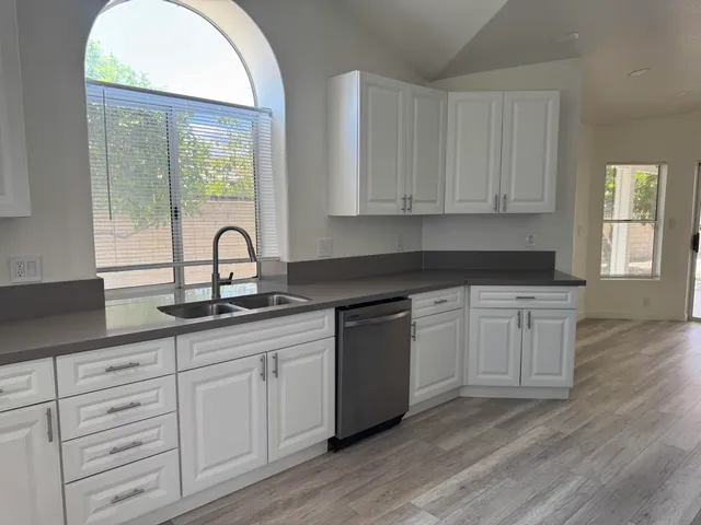 a kitchen with stainless steel appliances granite countertop a refrigerator a sink dishwasher and white cabinets with wooden floor
