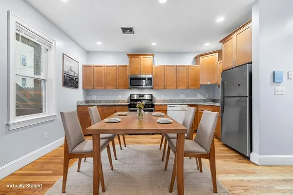 a kitchen with stainless steel appliances kitchen island granite countertop a dining table chairs and a refrigerator