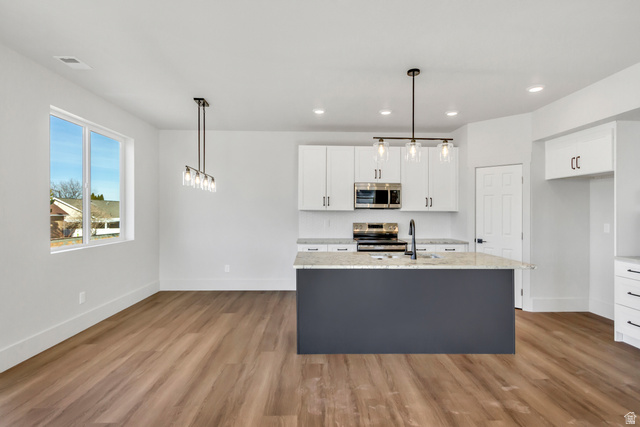 547 North Hvn Drive Mapleton, UT 84664 - Photo 6 of 23 Two tone kitchen featuring stainless steel appliances, decorative light fixtures, light stone countertops, a center island with sink, and light wood-type flooring