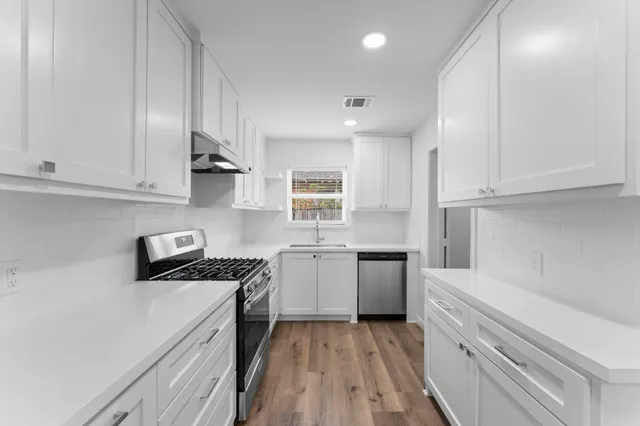 a kitchen with stainless steel appliances granite countertop white cabinets and a stove top oven