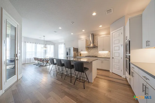 a kitchen with a dining table chairs wooden floor appliances and cabinets