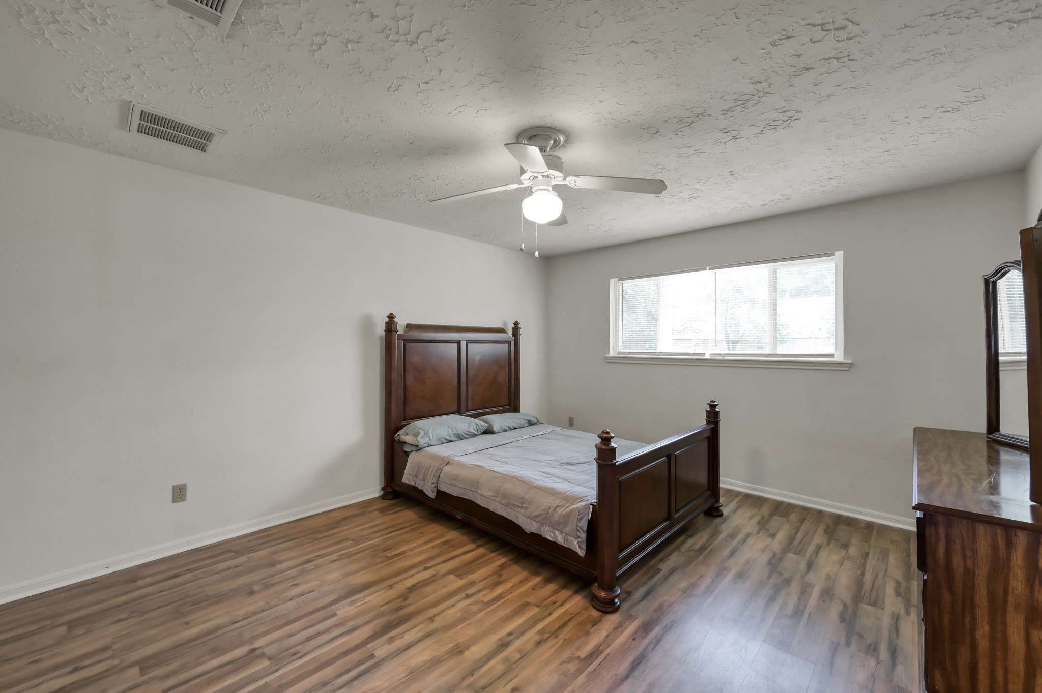 4314 Enchantedgate Drive Spring, TX 77373 - Photo 22 of 47 Primary bedroom features a large window for natural light, a ceiling fan, wood flooring, and ample space for furniture. The room has a neutral color palette, offering a versatile backdrop for personal decor.