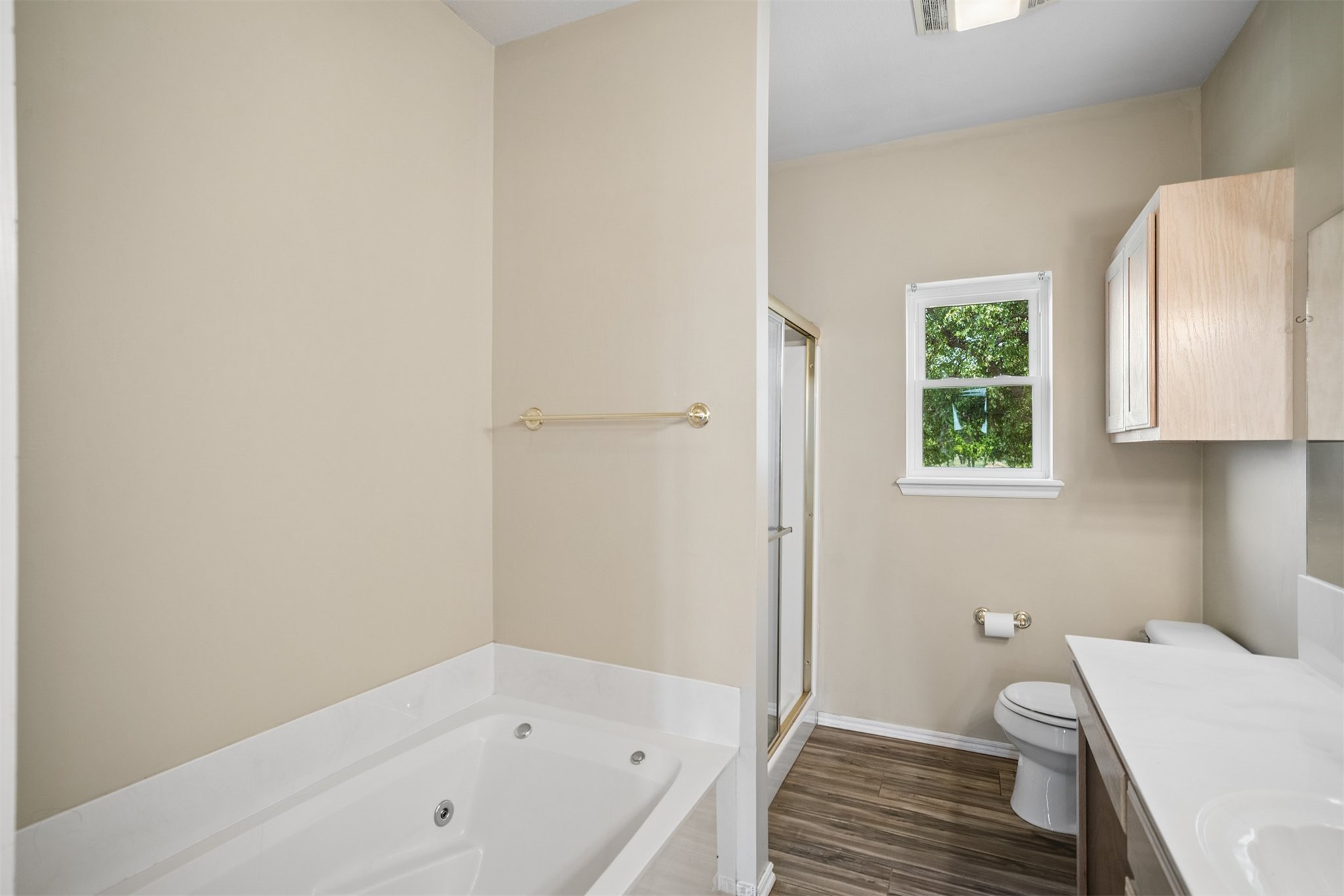 175 Alt 75 Mounds, OK 74047 - Photo 13 of 41 Soaking tub, walk-in shower with gold-tone frame, single vanity with white countertop, wood-finish flooring, and natural light