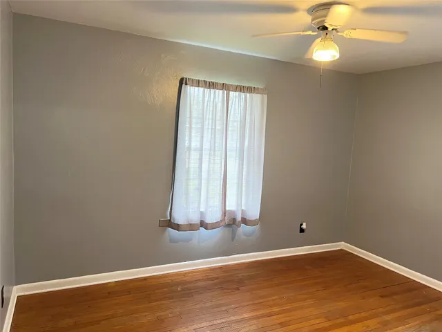 an empty room with wooden floor fan and window