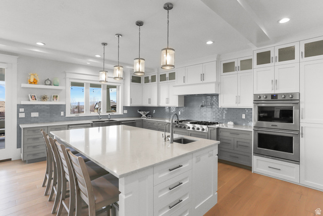 1354 South 800 East Mapleton, UT 84664 - Photo 6 of 129 Two tone kitchen featuring stainless steel appliances, a breakfast bar, light stone countertops, a kitchen island with sink, and light wood-style flooring