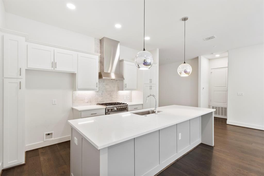 15875 Spectrum Drive, Unit 1106 Addison, TX 75001 - Photo 10 of 39 Kitchen featuring white cabinets, wall chimney range hood, backsplash, hanging light fixtures, and a center island with sink