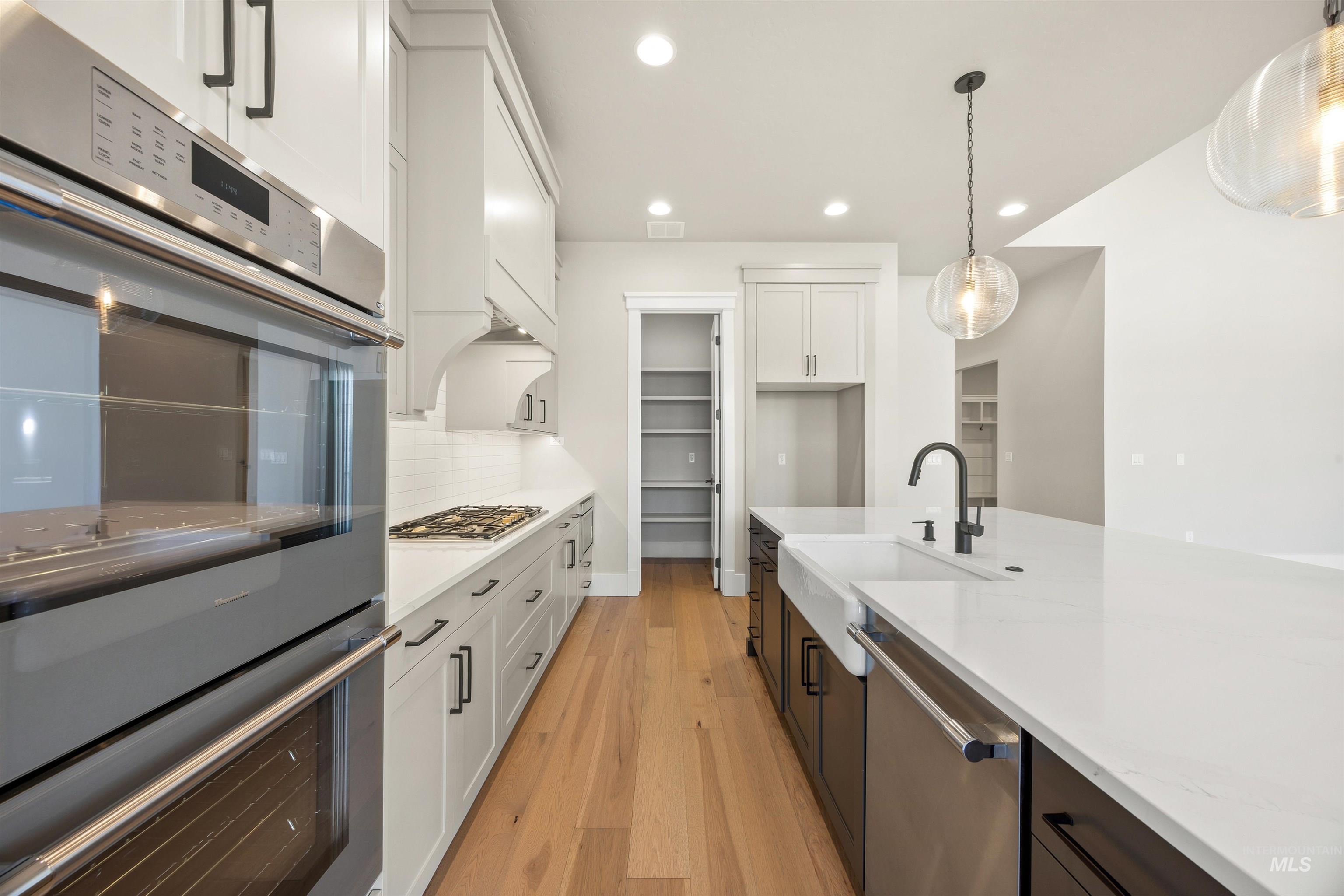 1126 East Crescendo Street Meridian, ID 83642 - Photo 16 of 48 Dual tone kitchen featuring stainless steel appliances, dual tone cabinetry, light wood-type flooring, pendant lighting, and light stone countertops