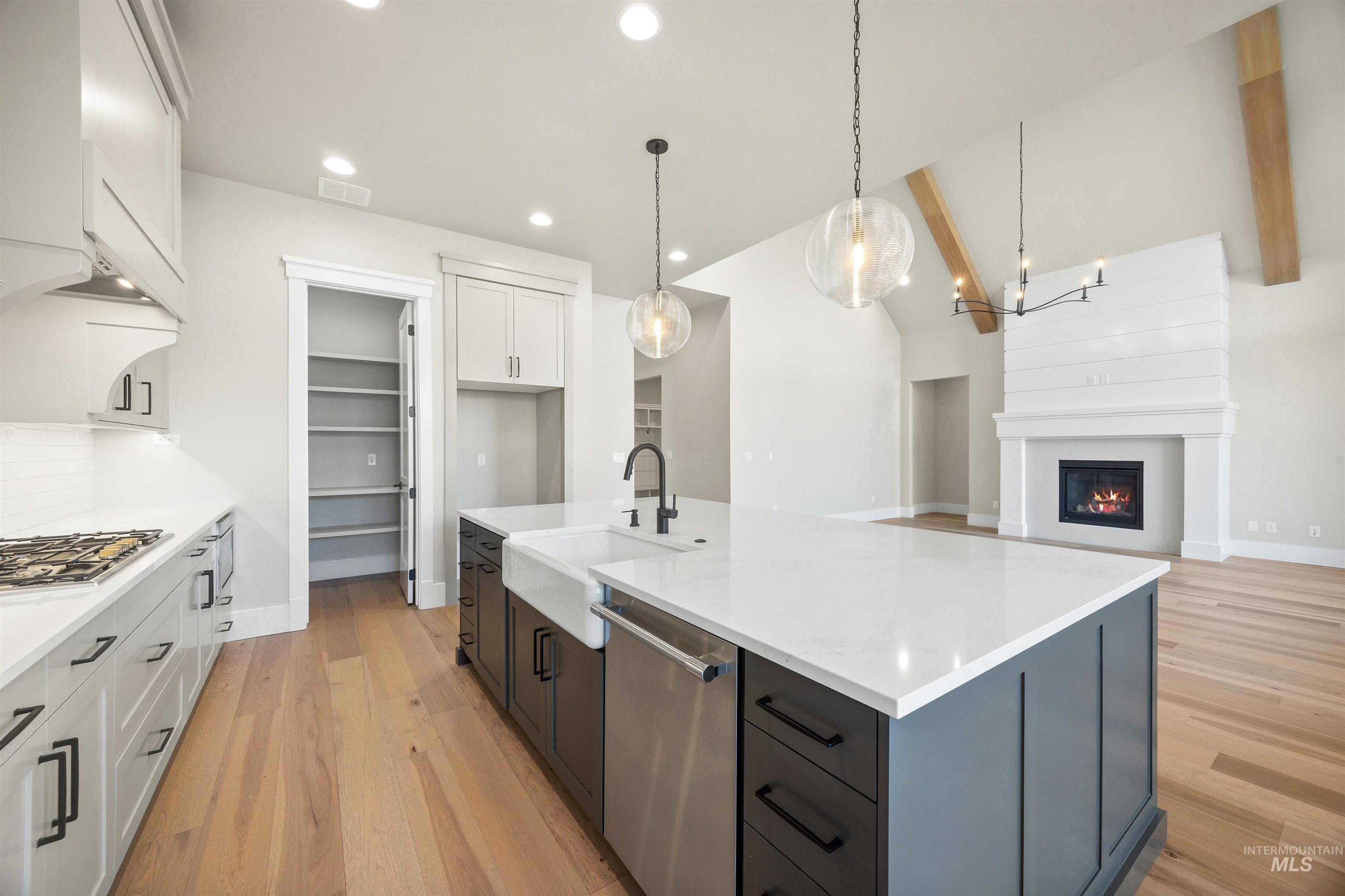 1126 East Crescendo Street Meridian, ID 83642 - Photo 17 of 48 Dual tone kitchen with dual tone cabinetry, light wood finished floors, decorative light fixtures, a kitchen island with sink, and stainless steel appliances