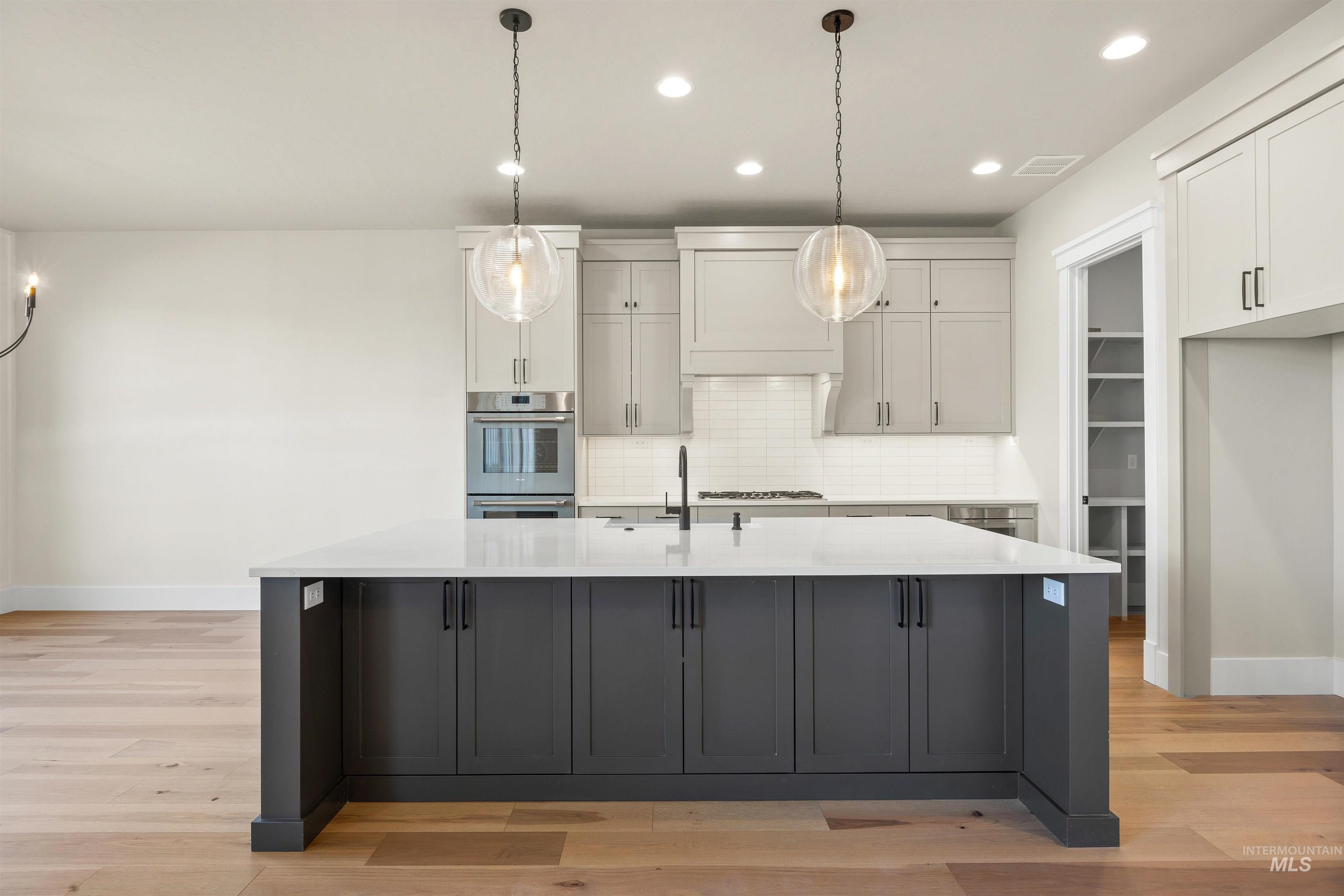 1126 East Crescendo Street Meridian, ID 83642 - Photo 20 of 48 Kitchen featuring two tone cabinets, pendant lighting, a large island, tasteful backsplash, and light wood finished floors