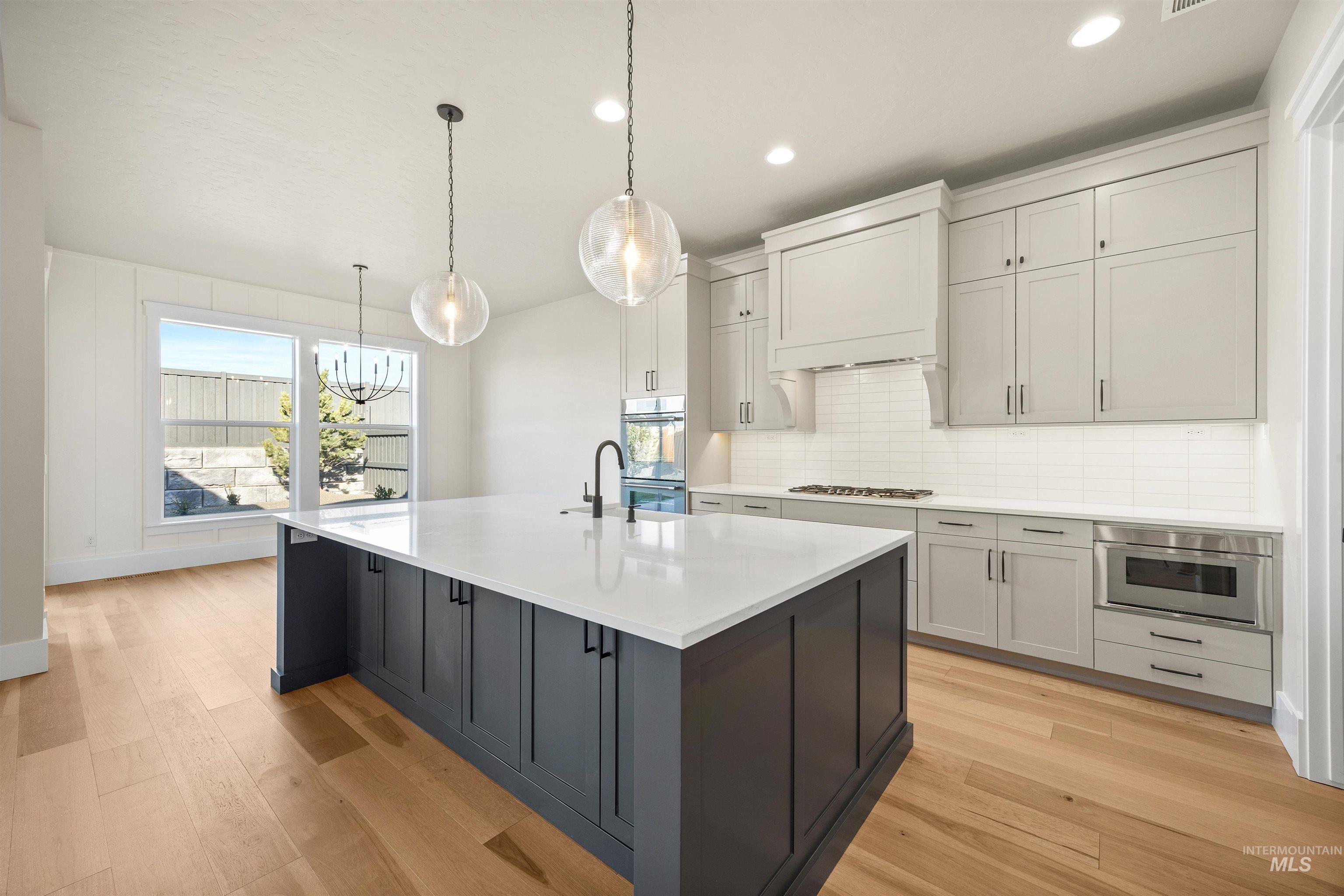 1126 East Crescendo Street Meridian, ID 83642 - Photo 22 of 48 Dual tone kitchen with two tone color scheme, light wood-style flooring, a kitchen island with sink, light stone countertops, and backsplash