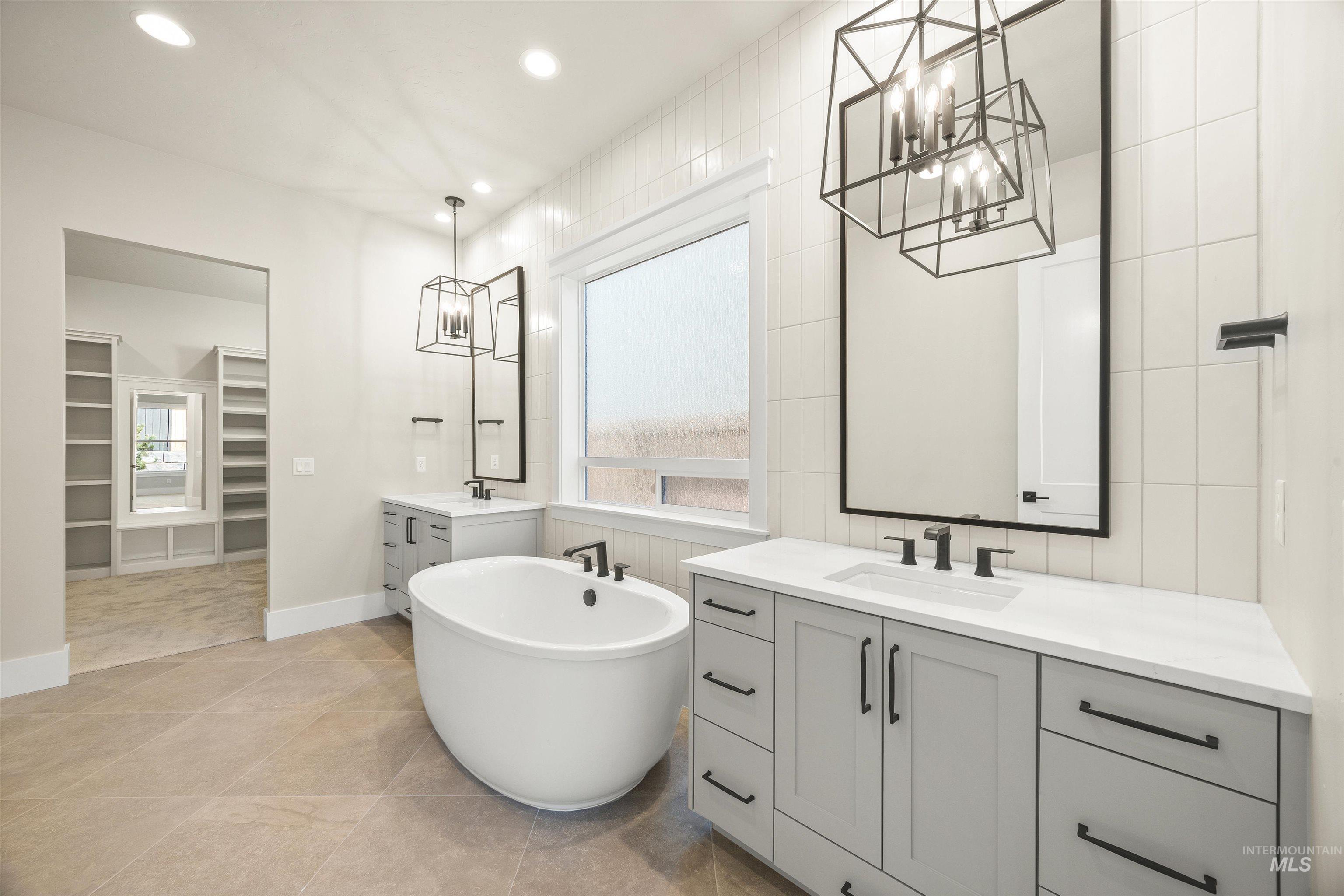 1126 East Crescendo Street Meridian, ID 83642 - Photo 31 of 48 Bathroom with two vanities, a walk in closet, a soaking tub, suspended lighting, and tile walls