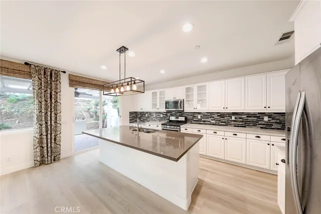 a kitchen with stainless steel appliances granite countertop a stove a sink dishwasher a refrigerator and white cabinets with wooden floor