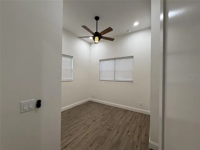 an empty room with wooden floor ceiling fan and windows