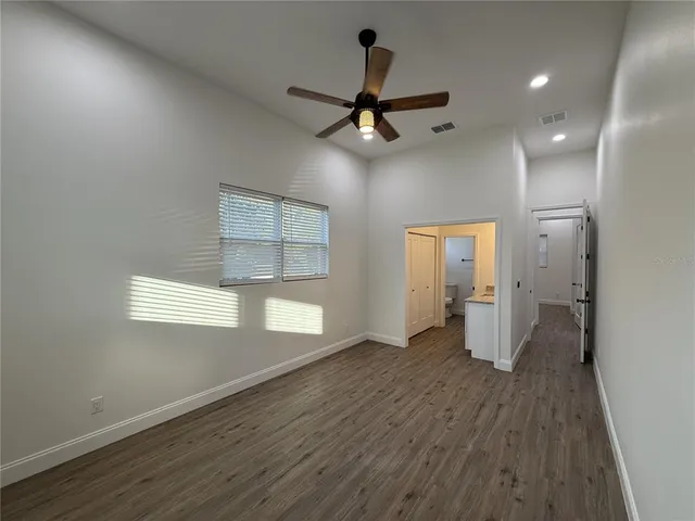 an empty room with wooden floor a ceiling fan and windows