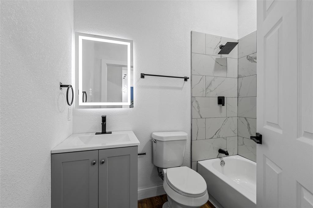 2023 Bosque Boulevard Waco, TX 76707 - Photo 19 of 26 Bathroom featuring a gray vanity with an integrated sink, an illuminated mirror, and a tiled shower with matte black fixtures