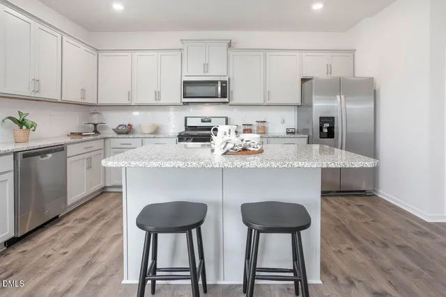 a kitchen with stainless steel appliances granite countertop a refrigerator a stove a sink dishwasher and white cabinets with wooden floor