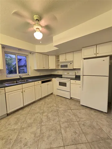 a kitchen with granite countertop a refrigerator a sink and white cabinets