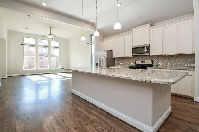 a kitchen with stainless steel appliances granite countertop a sink a stove a refrigerator a center island and wooden floor