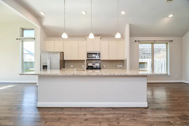 a large kitchen with granite countertop a large white kitchen island white cabinets and stainless steel appliances