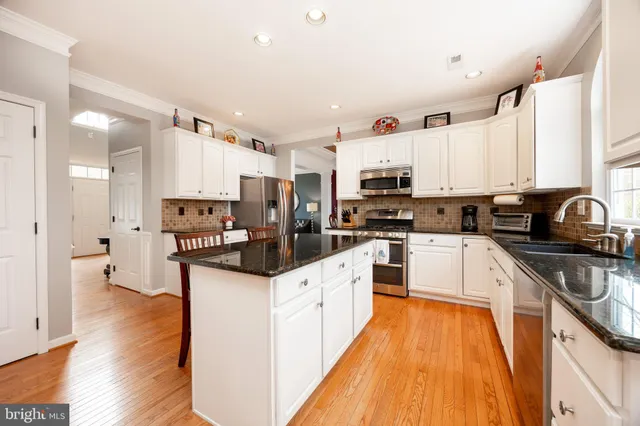 a kitchen with stainless steel appliances kitchen island granite countertop a stove a sink a refrigerator and white cabinets with wooden floor