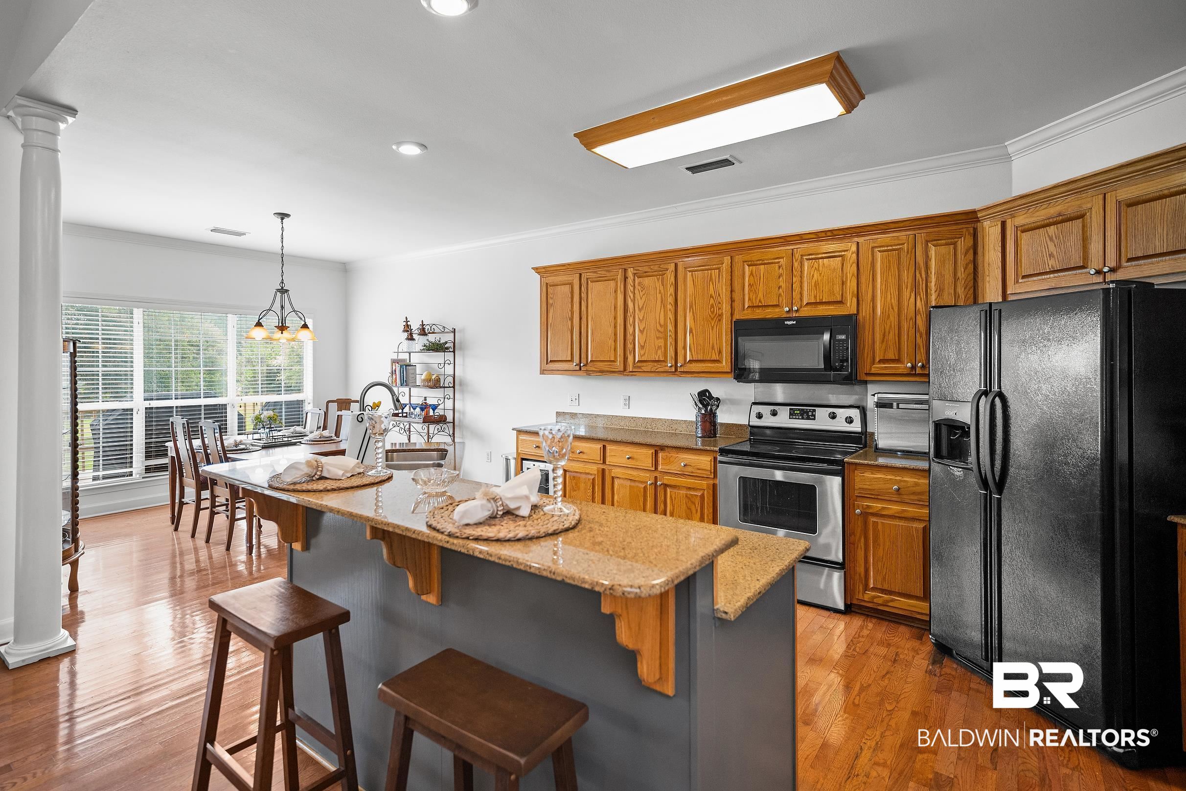 197 Morning Ridge Road Monroeville, AL 36460 - Photo 12 of 51 Kitchen featuring a granite-topped island with breakfast bar, wood-finish flooring, oak cabinetry, stainless steel appliances, and a dining area with pendant lighting and large windows