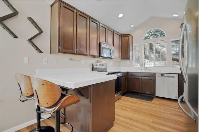a kitchen with stainless steel appliances granite countertop a sink dishwasher and a refrigerator with wooden cabinets