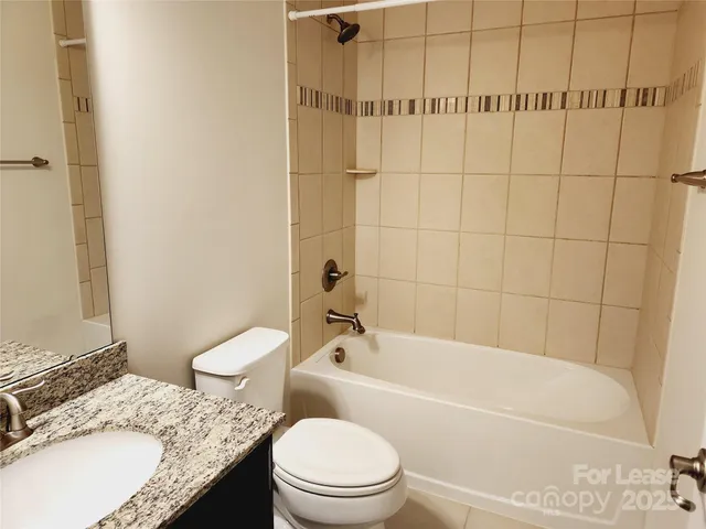 a bathroom with a granite countertop bathtub shower sink mirror vanity and toilet