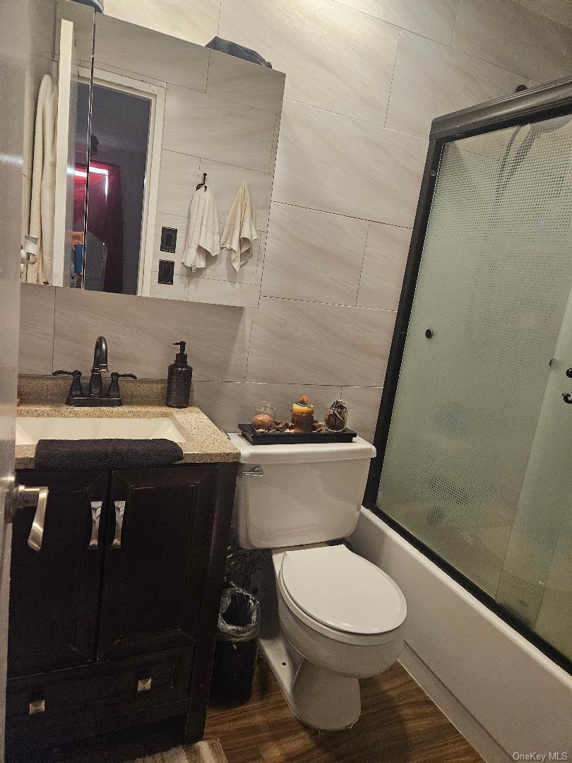 2 Richmond Road, Unit 4F Lido Beach, NY 11561 - Photo 10 of 26 Full bathroom with vanity, dark finished floors, bath / shower combo with glass door, tile walls, and backsplash