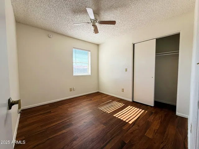 a view of an empty room with wooden floor and a ceiling fan