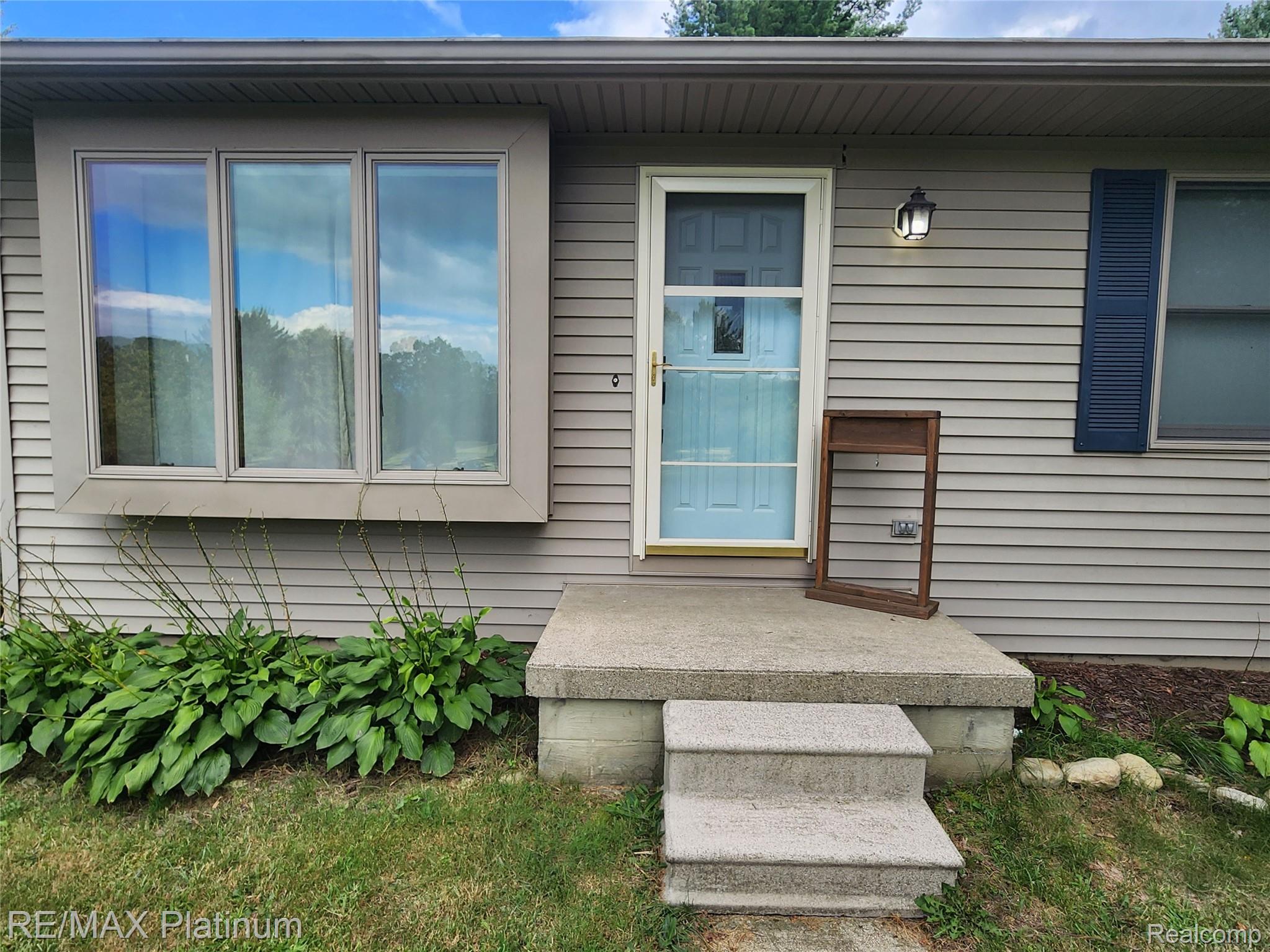 6451 Bullard Road Fenton, MI 48430 - Photo 1 of 26 Gray siding exterior with a light blue entry door, a storm door, and a bay window