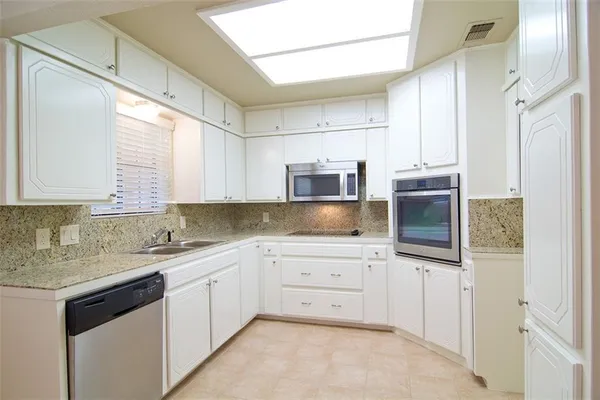a kitchen with stainless steel appliances granite countertop a sink and dishwasher a refrigerator with white cabinets