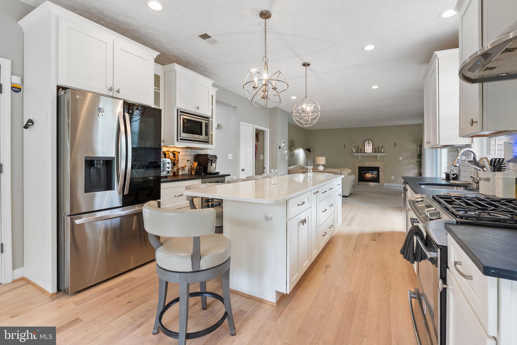 3207 Breckenridge Way Riva, MD 21140 - Photo 5 of 51 a large white kitchen with stainless steel appliances kitchen island granite countertop a stove a refrigerator a oven a dining table and chairs with wooden floor