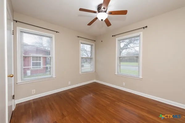 an empty room with wooden floor ceiling fan and windows