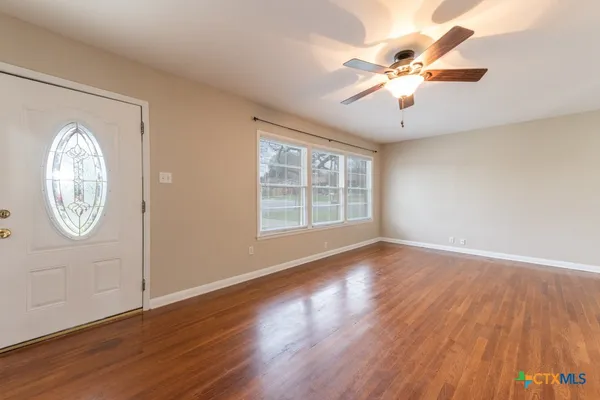 an empty room with wooden floor fan and windows