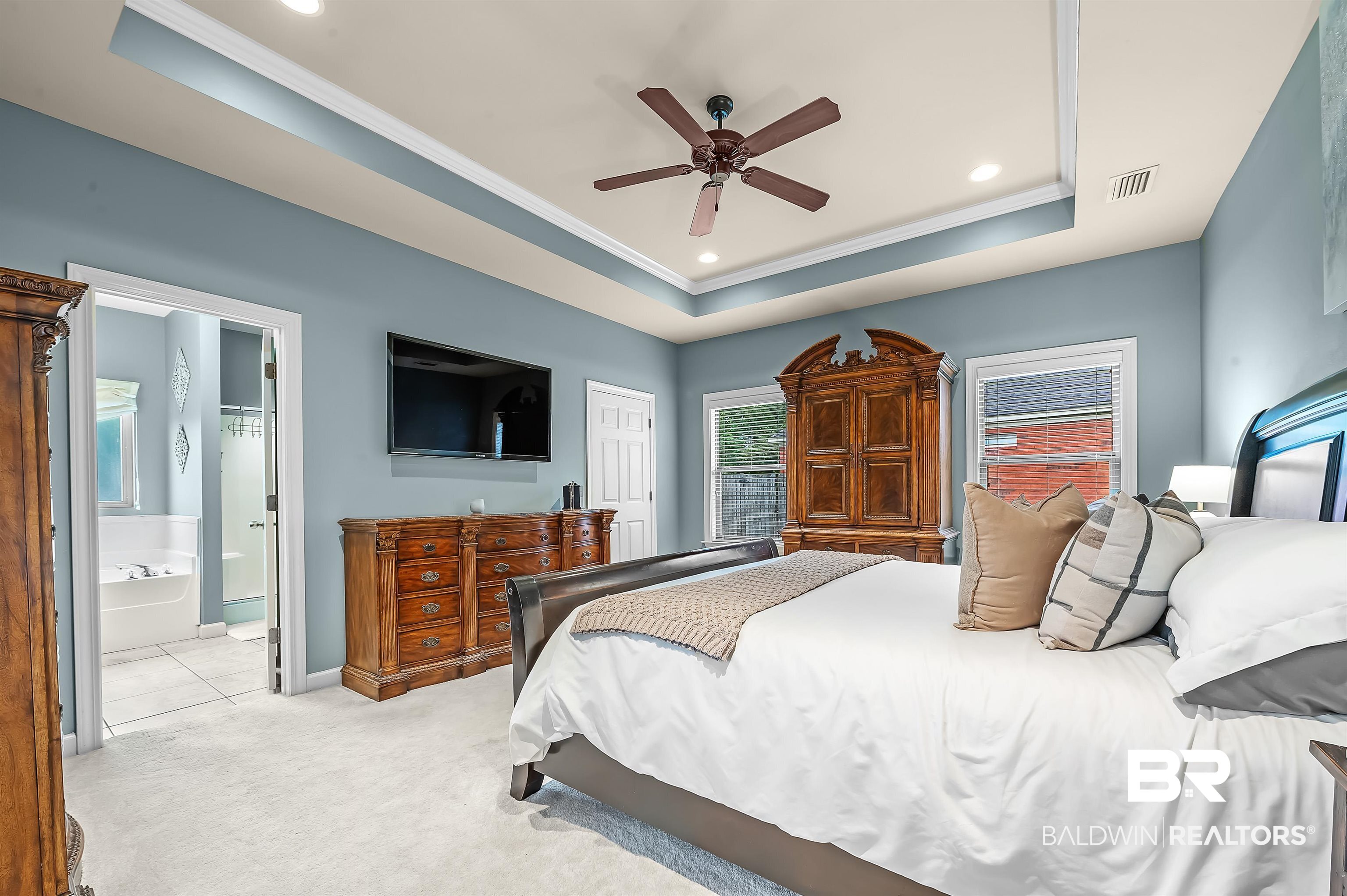 9376 Sable Court Daphne, AL 36526 - Photo 24 of 46 Bedroom featuring light carpet, a tray ceiling, crown molding, connected bathroom, and ceiling fan