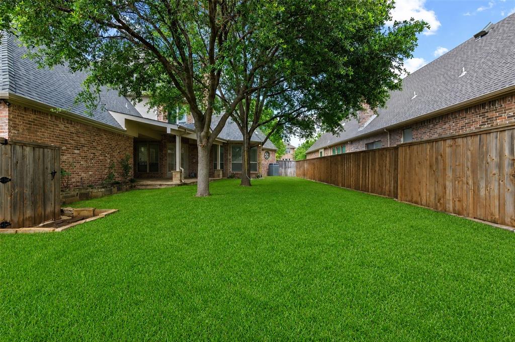 967 East Bethel School Road Coppell, TX 75019 - Photo 36 of 39 Spacious backyard featuring a lush lawn, mature trees, a covered patio, brick exterior, and a privacy fence. s