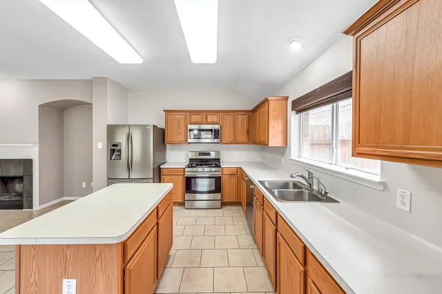 a kitchen with stainless steel appliances a sink a stove a refrigerator cabinets and a window