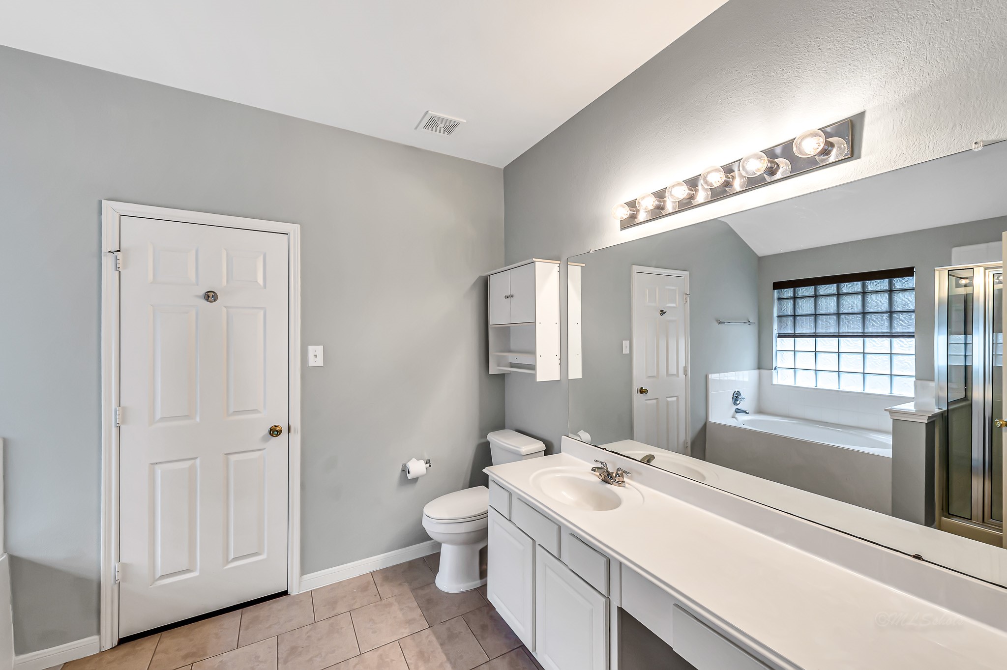 1602 Rustic Hollow Lane Katy, TX 77450 - Photo 22 of 48 Spacious primary bath featuring a long double-sink vanity, separate shower, relaxing soaking tub with glass-block window for natural light, and ample storage. Neutral finishes and a bright, clean layout create a comfortable and functional space.