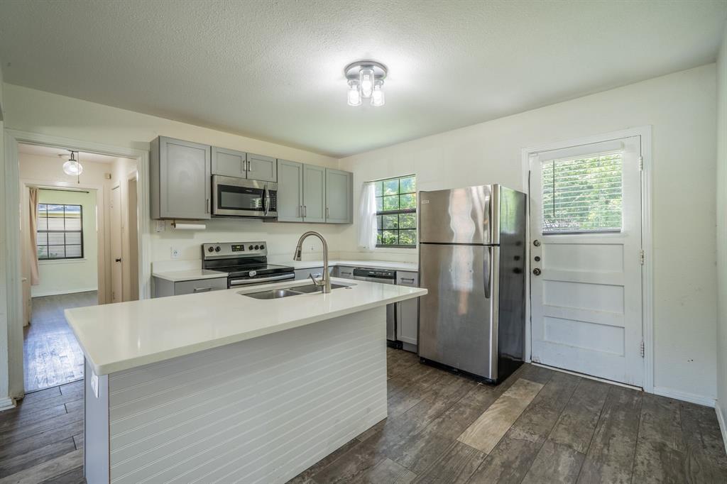 11528 Sinclair Avenue Dallas, TX 75218 - Photo 5 of 16 Kitchen featuring an island with a white countertop, stainless steel appliances, gray cabinetry, and wood-finish flooring