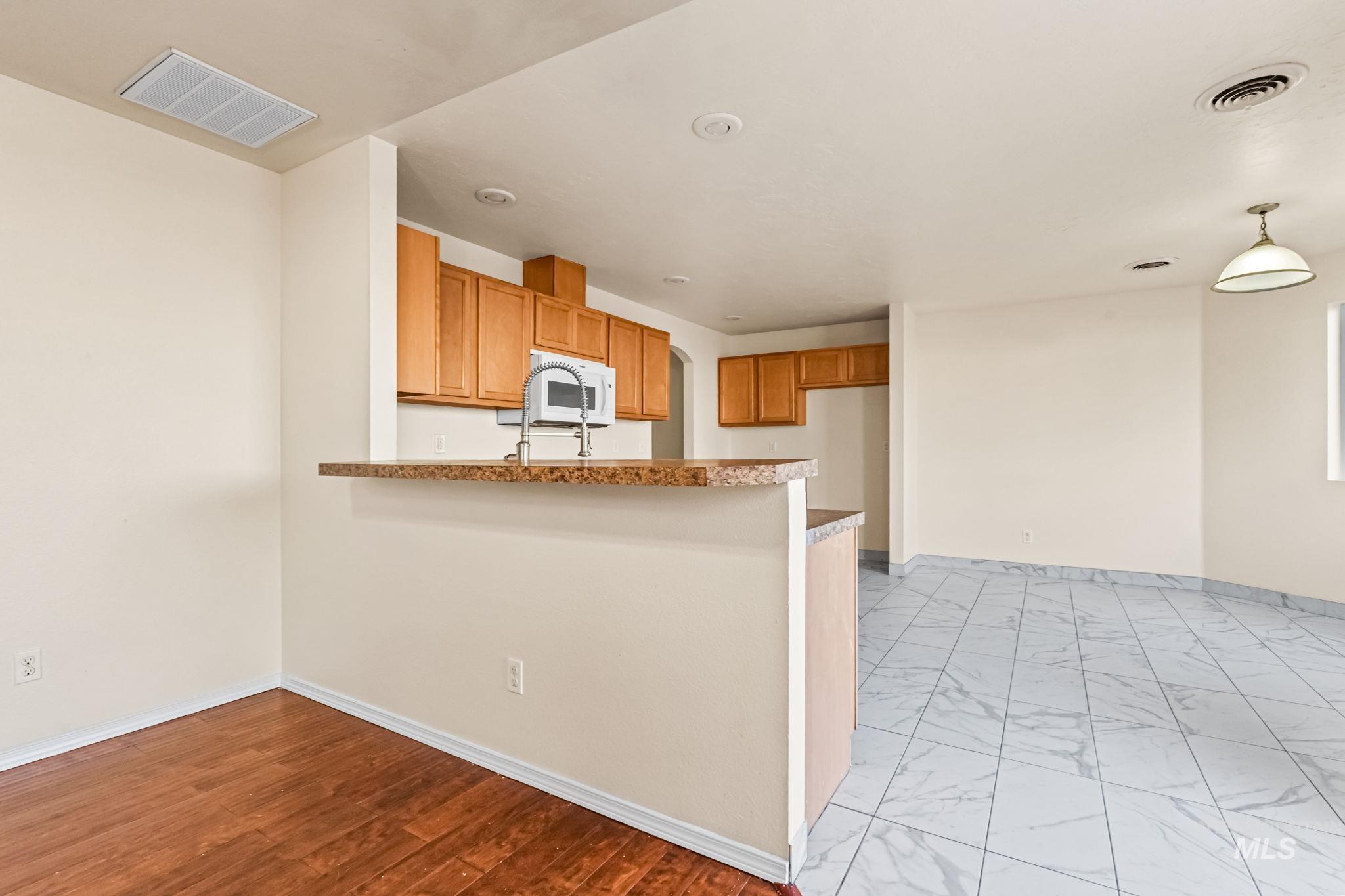 4523 Duke Street Caldwell, ID 83607 - Photo 9 of 27 Kitchen featuring a peninsula, brown cabinetry, white microwave, decorative light fixtures, and light marble finish floors