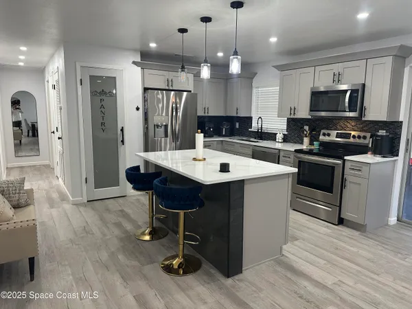 a large kitchen with stainless steel appliances kitchen island granite countertop a sink a stove a refrigerator and a dining table with wooden floor